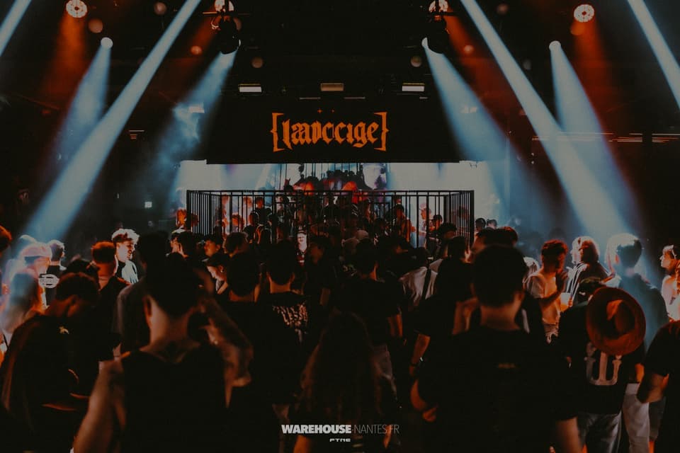 Soirée Hardcage au Warehouse Nantes : cage centrale sur le dancefloor sous la bannière au logo, beams blancs en V, wash ambre