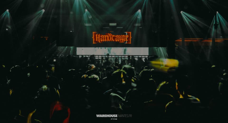 Douches de spots depuis le gril et logo Hardcage orange sur un look teal sombre, Warehouse Nantes